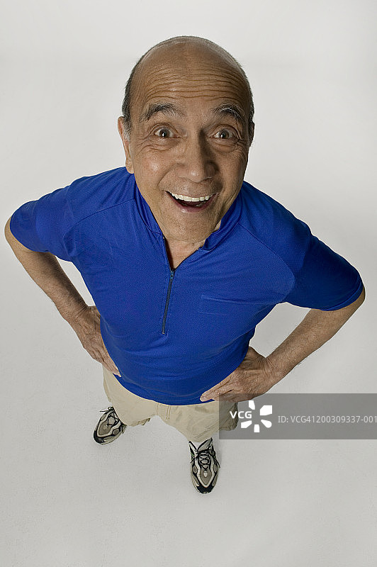 双手叉腰，在工作室摆姿势的年长男人肖像，仰视图片素材