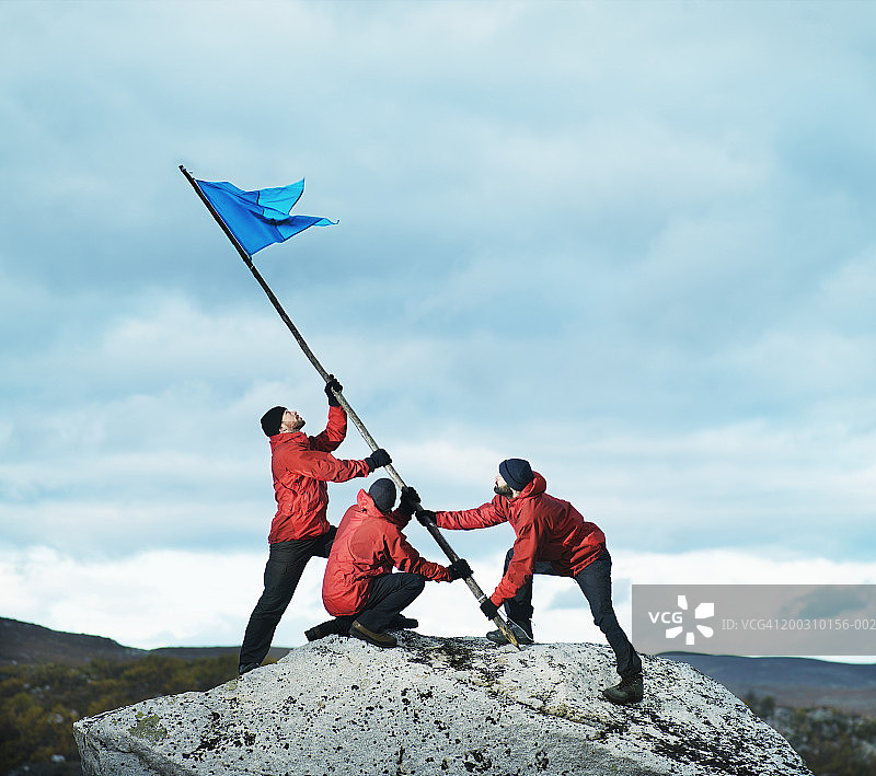 三名男性徒步者在岩石上挥旗图片素材