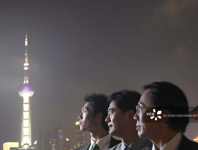 夜幕下远眺城市天际线的三位商人图片素材