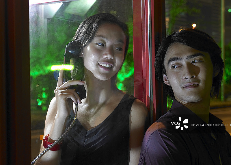 年轻女人在电话亭里对着年轻男人微笑，夜晚图片素材