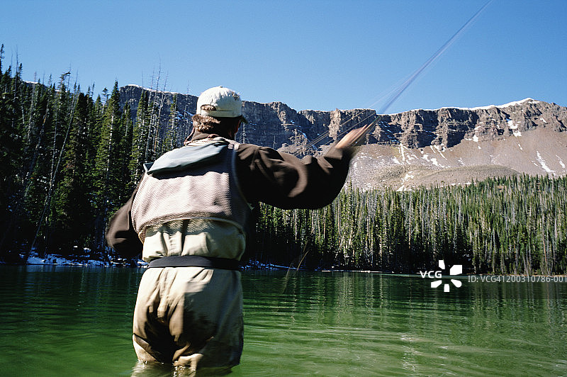 在高原湖泊飞蝇钓鱼的男人（后视图，动态模糊）图片素材