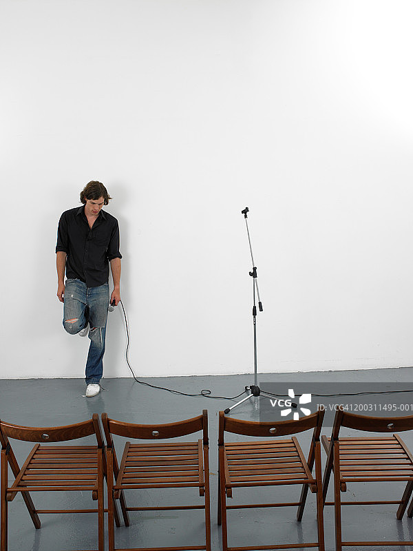 男人手持麦克风靠在空椅子前的墙上图片素材