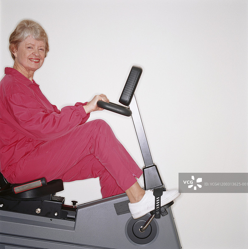 在健身车上踩踏板、在工作室摆姿势的年长女性肖像图片素材