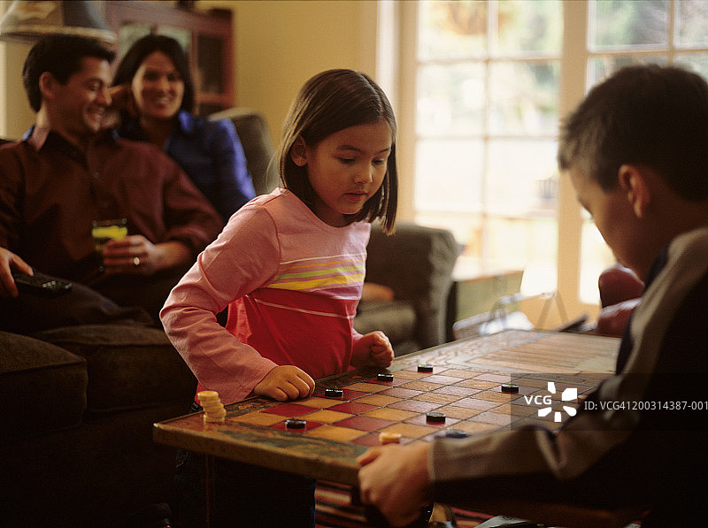 兄妹(6-7岁)，(8-9岁)在客厅里玩跳棋，父母坐在沙发上图片素材