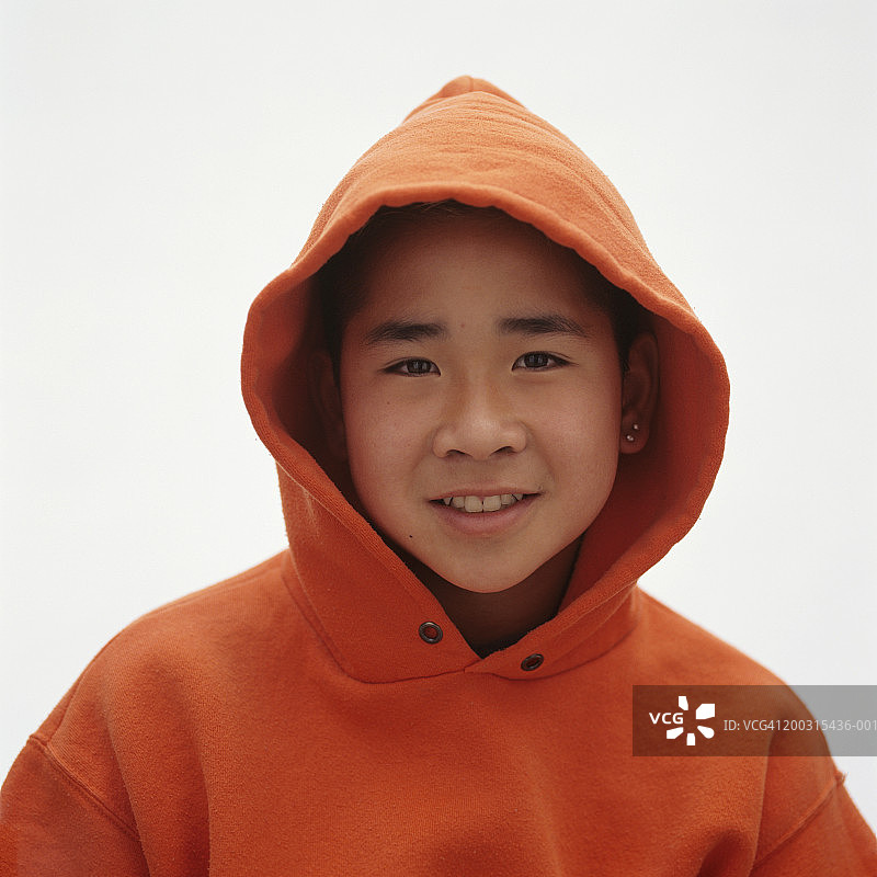 穿着橙色连帽上衣，在工作室摆姿势的青少年男孩（14-15岁），肖像图片素材