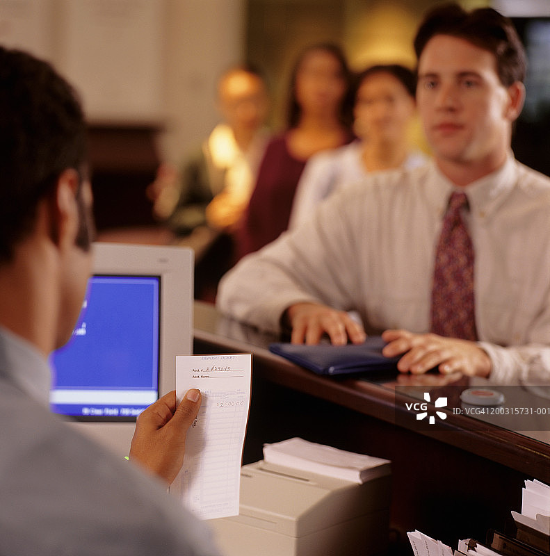 年轻男人在银行柜台前，出纳员正在核对收据图片素材