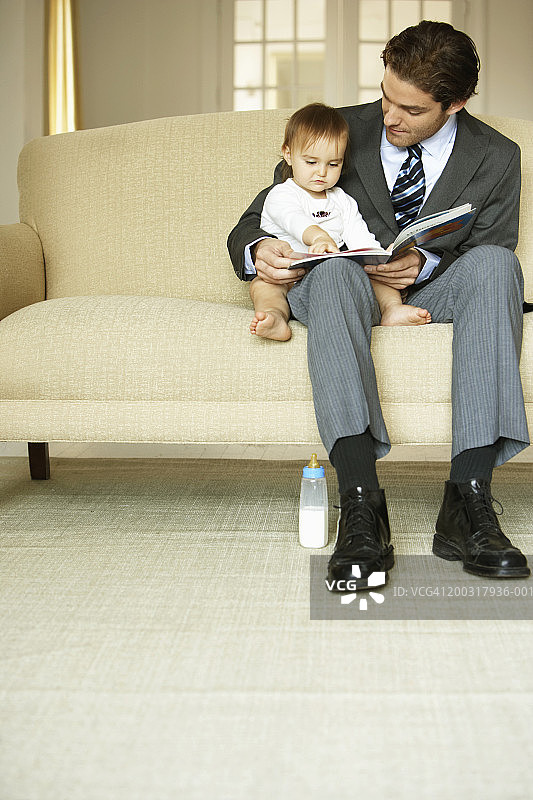 父亲在沙发上给女儿（15-18个月）读书图片素材