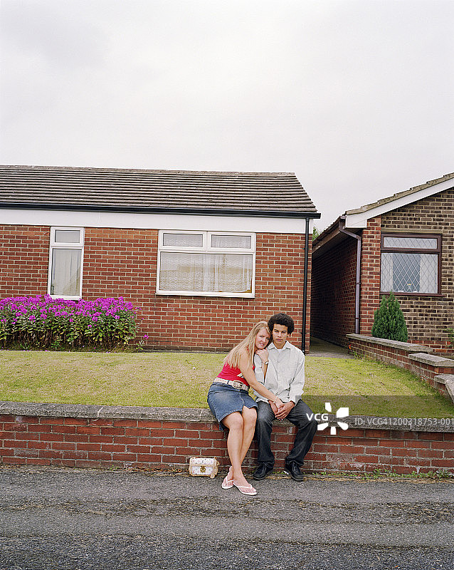 情侣坐在房子前的墙上，手牵着手图片素材