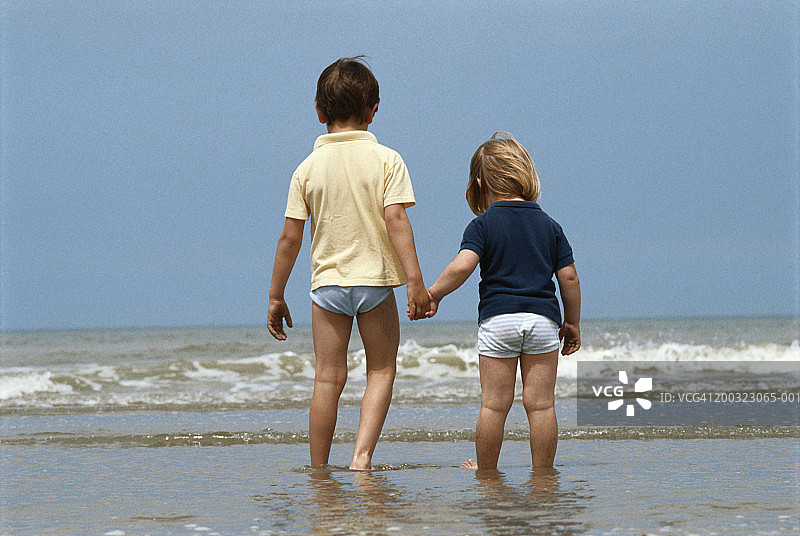 在海滩上牵手的男孩和女孩（3-5岁），后视图图片素材