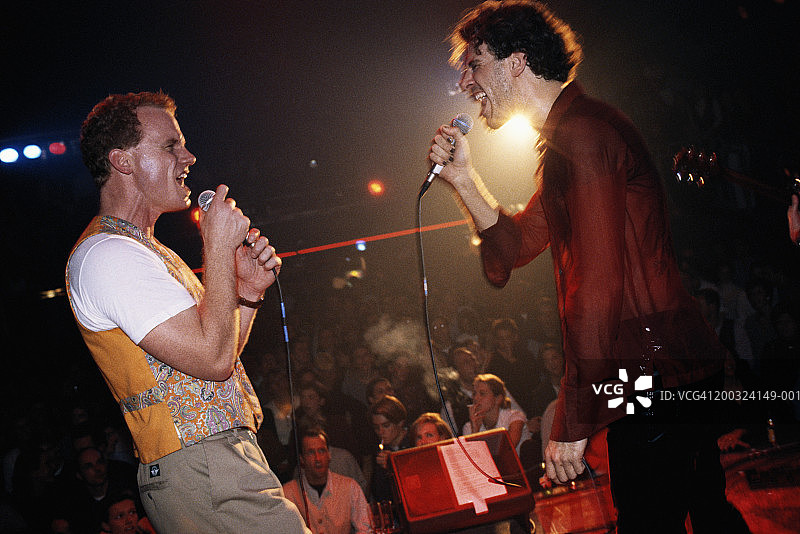 在音乐会上，两个男人面对面侧视着麦克风唱歌图片素材