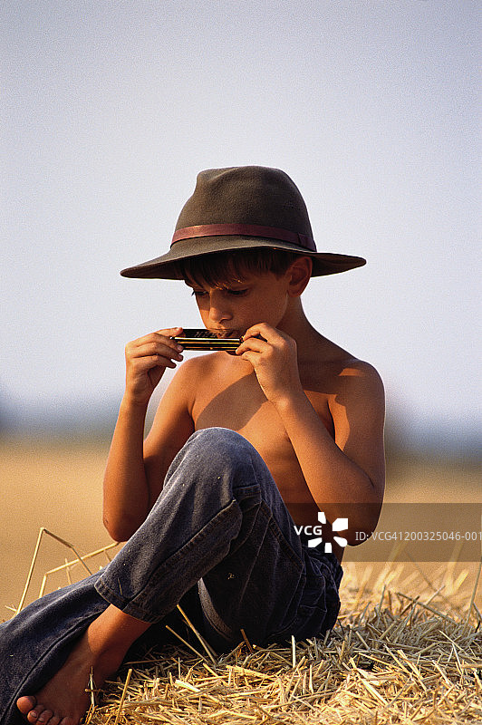 坐在干草堆上吹口琴的小男孩（8-9岁）图片素材