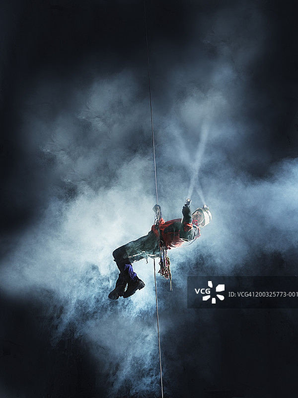 在洞穴中绳降的年长的男人，拿着火炬图片素材