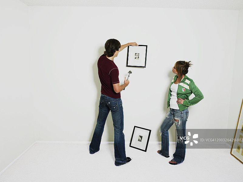 年轻男子将照片挂在墙上，女子在一旁观看图片素材