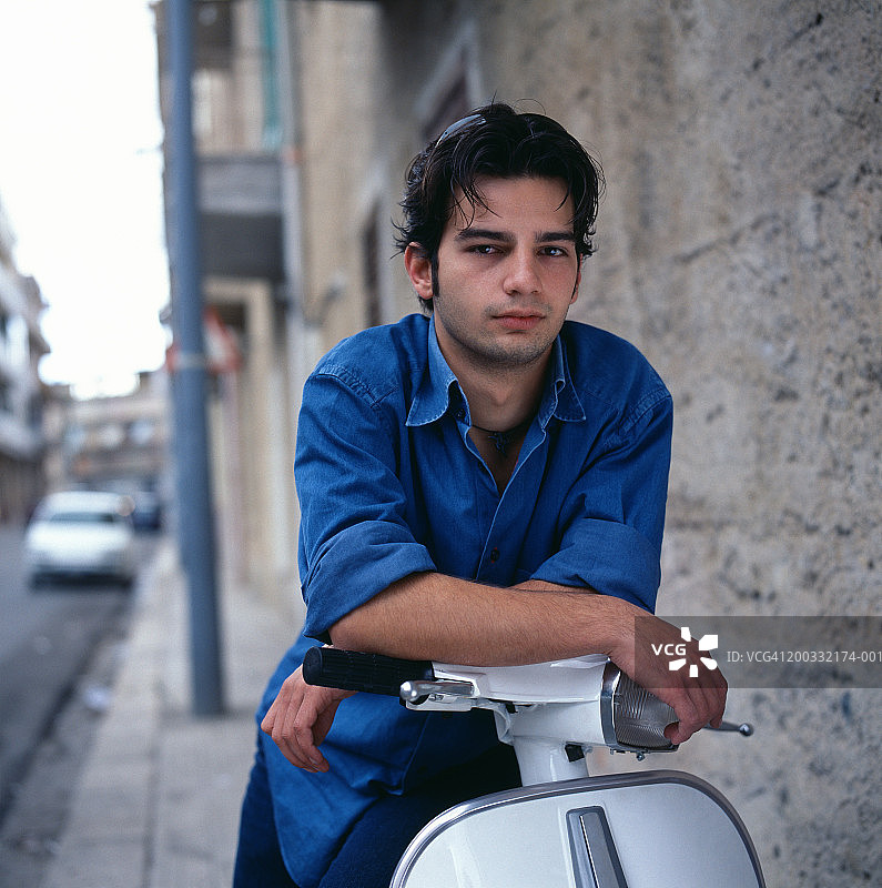 坐在人行道上的滑板车上的年轻男人肖像图片素材
