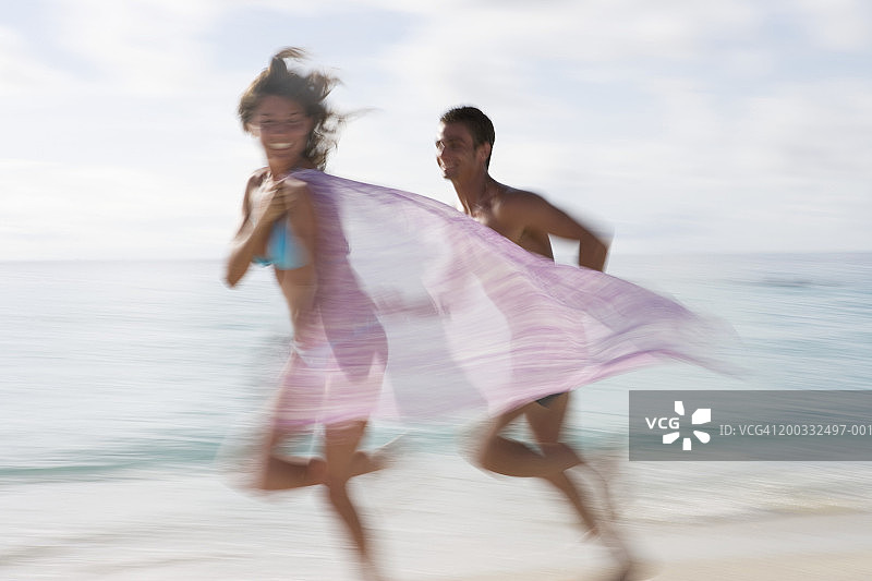 情侣在海滩奔跑，女人拖着面纱（动态模糊）图片素材