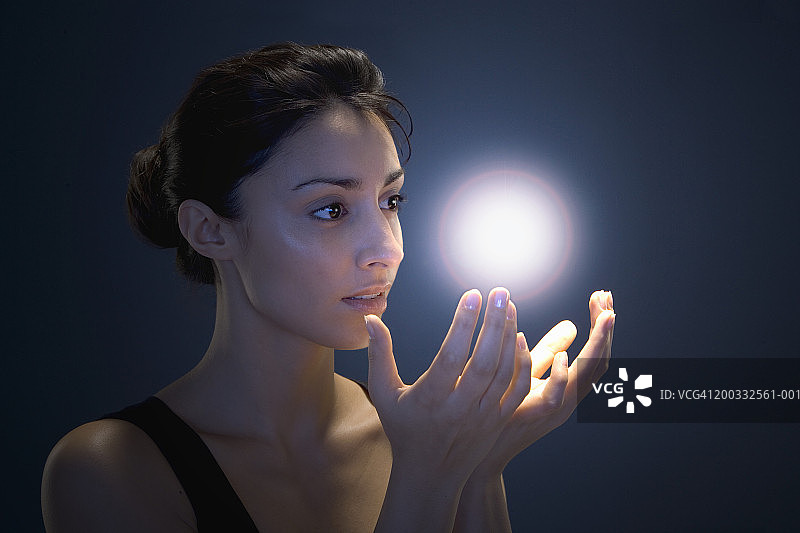 年轻女人用双手捧着发光球体（数码增强）图片素材