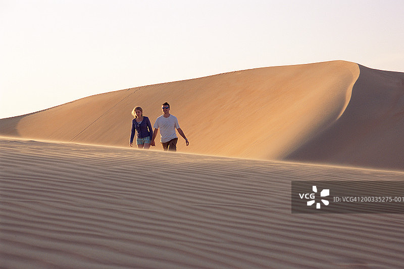 情侣在沙漠景观中牵手行走，微笑图片素材