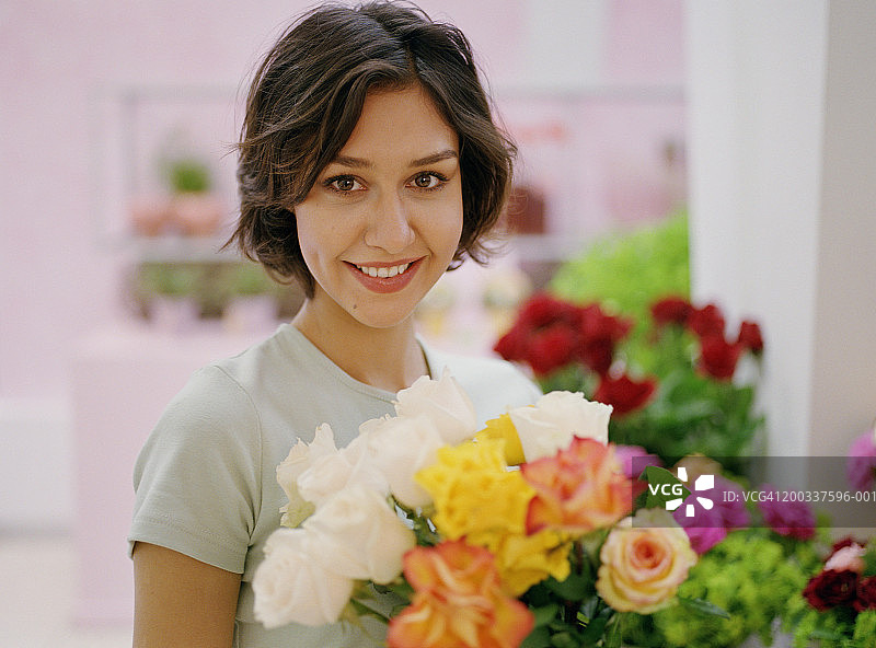 花店里手捧玫瑰花束的微笑女人肖像图片素材