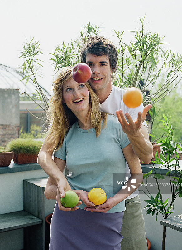 男子在阳台上与女子拥抱，抛着水果，面带微笑图片素材