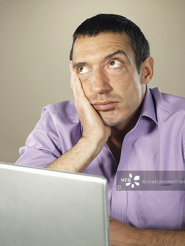 男人在使用笔记本电脑，手托着头，向上看图片素材