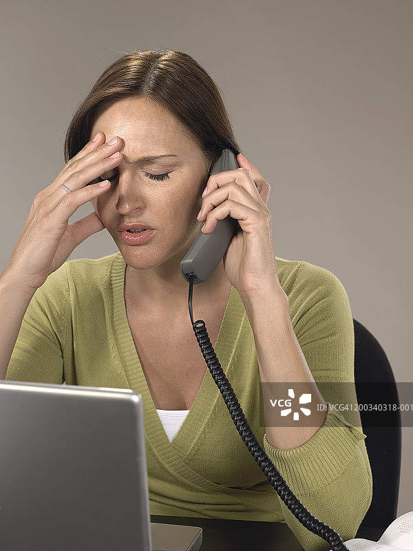 在桌旁用电话的女人，手扶着头，闭着眼睛图片素材