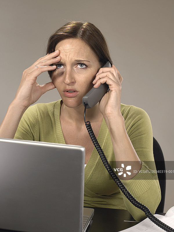 在办公桌前打电话的女人，手扶头部，向上看图片素材
