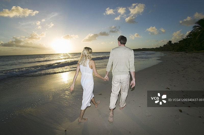 情侣在海滩上牵手散步，日落时分图片素材