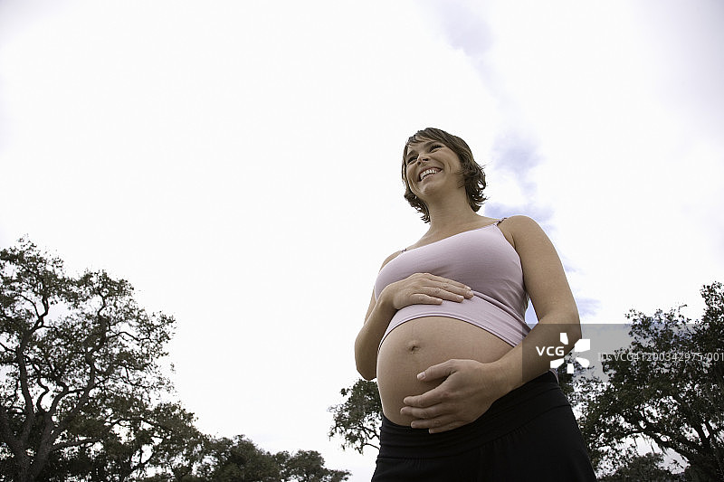 手扶肚子微笑的孕妇，低角度拍摄图片素材