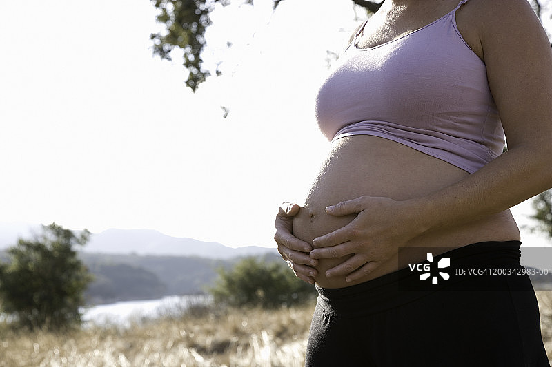 湖边的孕妇手抚肚子（侧面视角，身体中部）图片素材