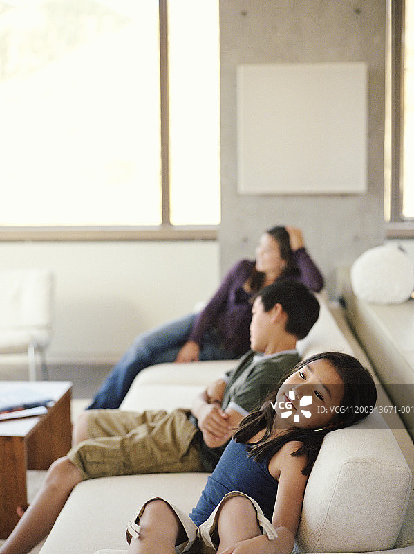坐在沙发上的三个兄弟姐妹（9-17岁）（焦点在前方的女孩身上）图片素材
