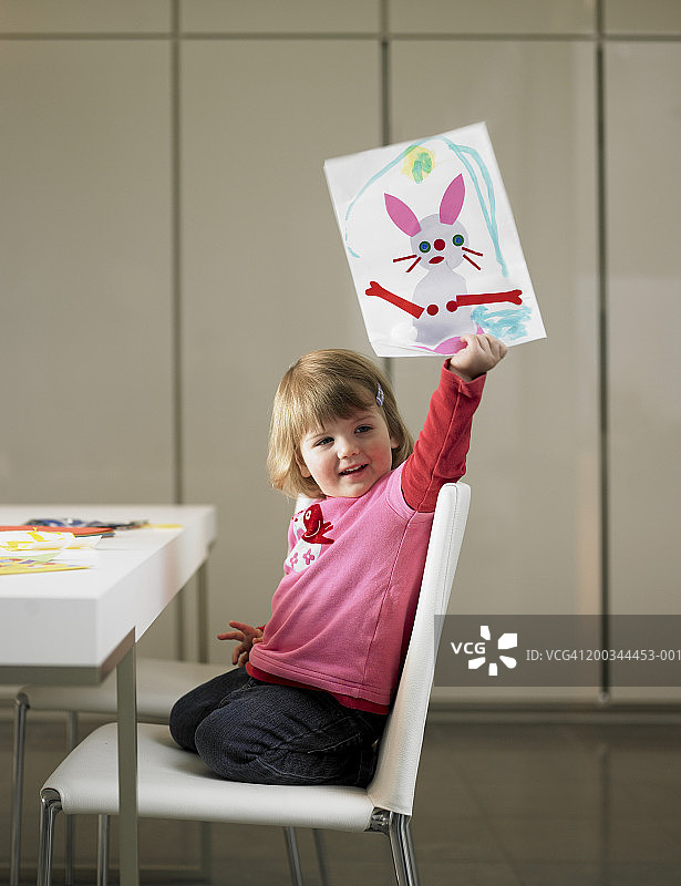 女孩（2-4岁）跪在椅子上，举着一张兔子照片图片素材
