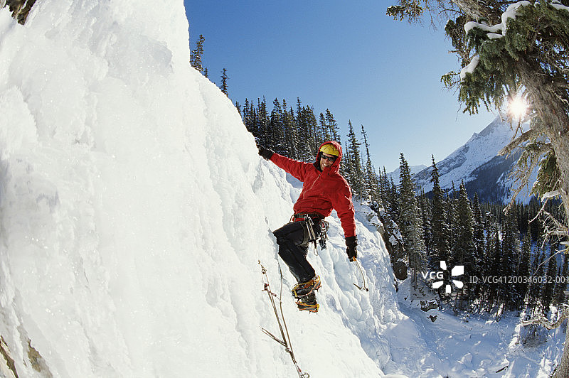 年轻男子攀登冰冻瀑布，面带微笑图片素材