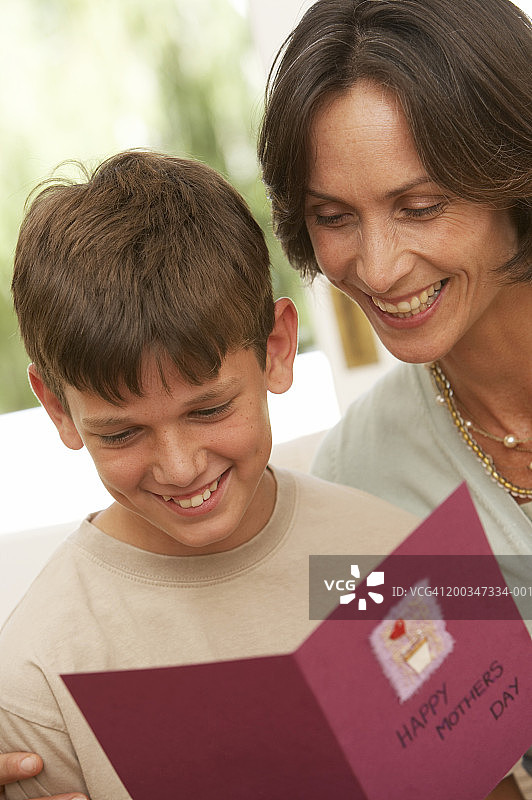 母亲和儿子(10-12岁)看着卡片，微笑图片素材