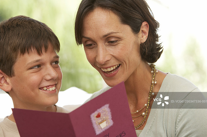 母亲和儿子（10-12岁）微笑，前景有卡片图片素材