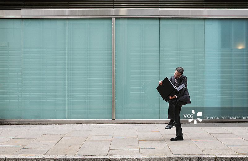 在人行道上打开公文包并使用手机的商人图片素材