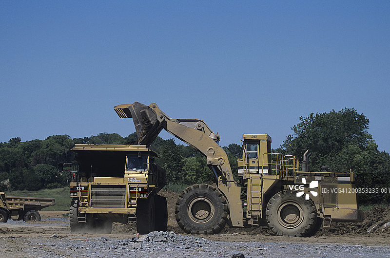 重型建筑道路施工：大型前端装载机向自卸卡车填充砂砾图片素材