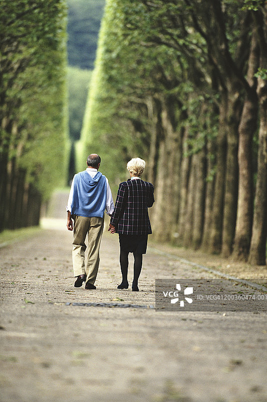 一对中年夫妇走在林荫小路上，背影视角图片素材