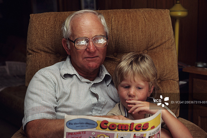 （4-5岁）坐在爷爷腿上读漫画的男孩图片素材