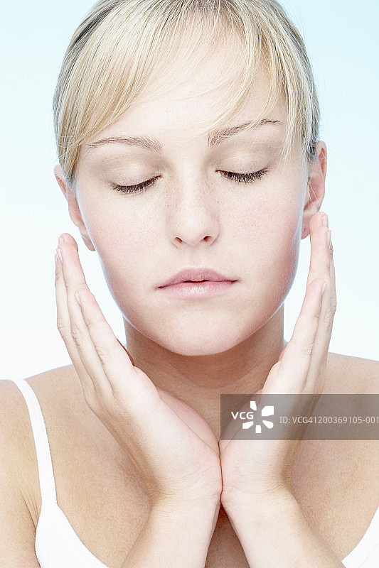 双手放在脸旁，闭着眼睛的年轻女人特写图片素材