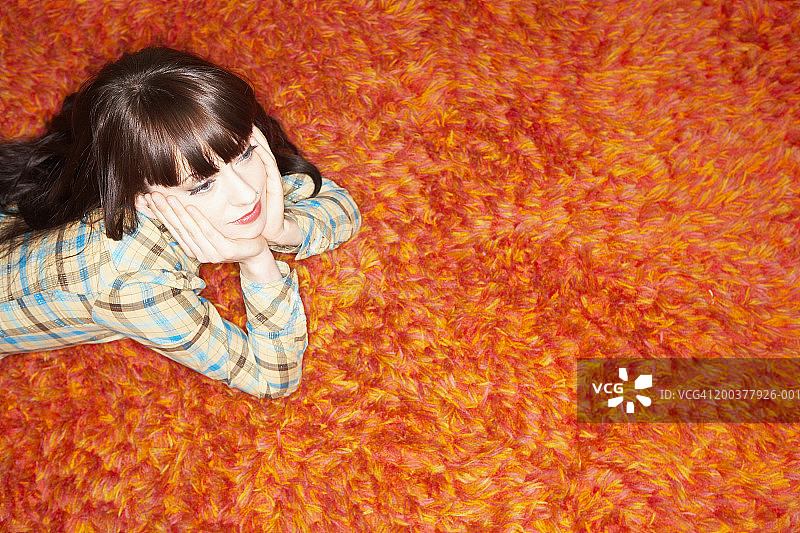 高角度拍摄的躺在长毛地毯上，下巴 resting 在手上的女人图片素材