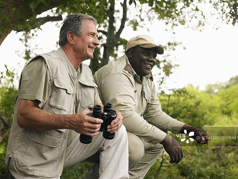 年长的男人拿着双筒望远镜，在导游的带领下进行狩猎，面带微笑图片素材