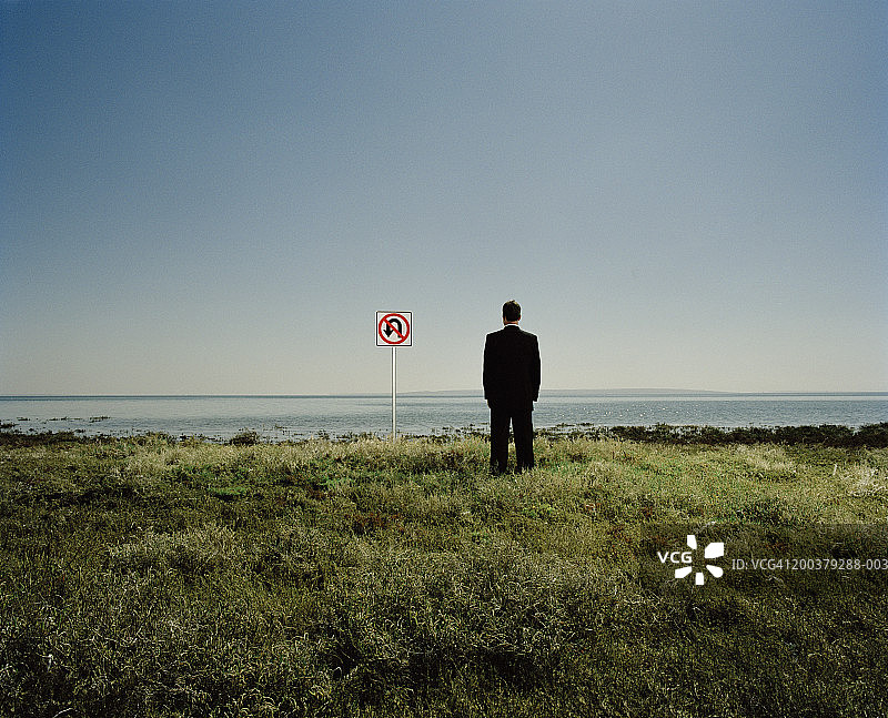 海洋边“禁止掉头”标志旁的商务人士（后视图）图片素材