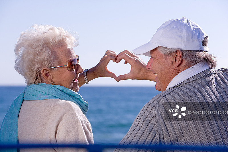 老年夫妇在海边用手比心微笑图片素材