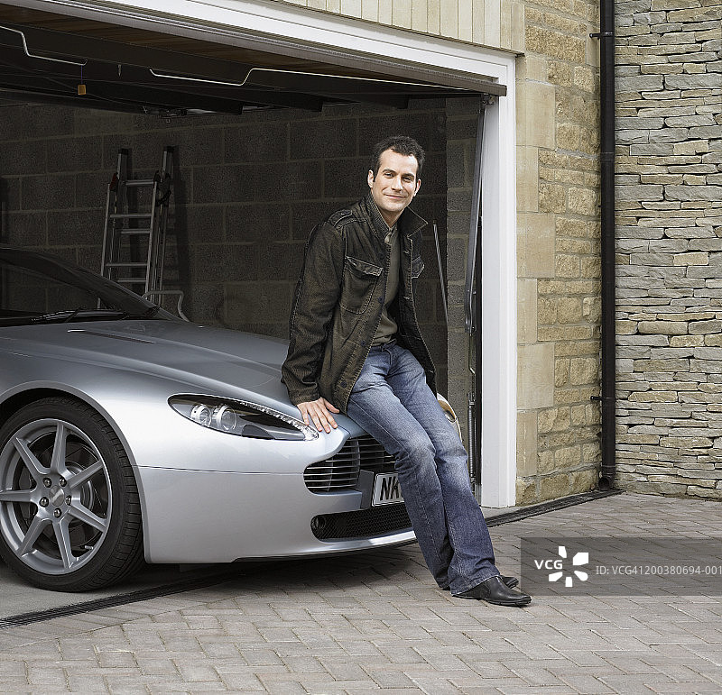 坐在车库汽车上的微笑年轻男人肖像图片素材