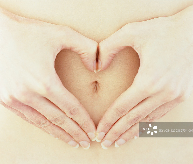 女人用手在肚脐周围比心形，特写图片素材