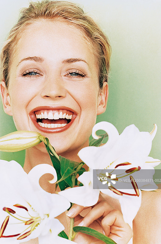 年轻女人手持百合花，笑着，特写肖像图片素材