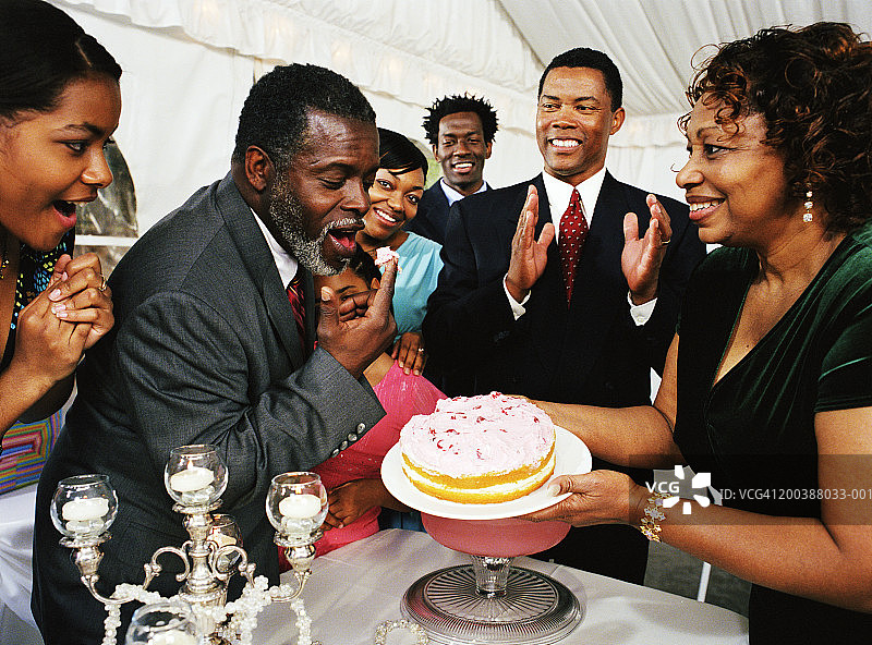 在家庭庆祝活动中品尝蛋糕糖霜的中年男人图片素材