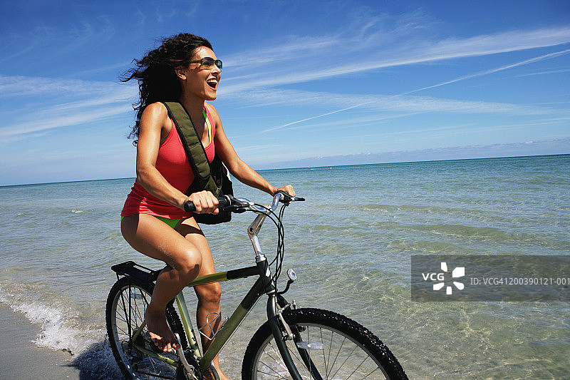 在海滩上骑自行车的年轻女子，面带微笑，侧面视角图片素材