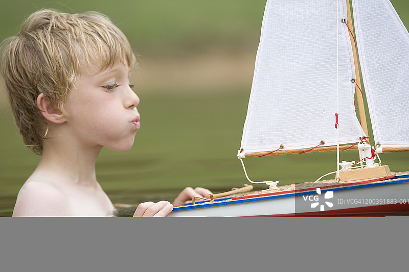 4-6岁男孩在湖中玩帆船，侧视图图片素材