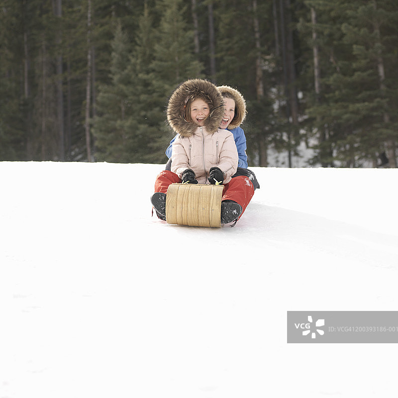 两个女孩（9-11岁）在山坡上玩平底雪橇图片素材
